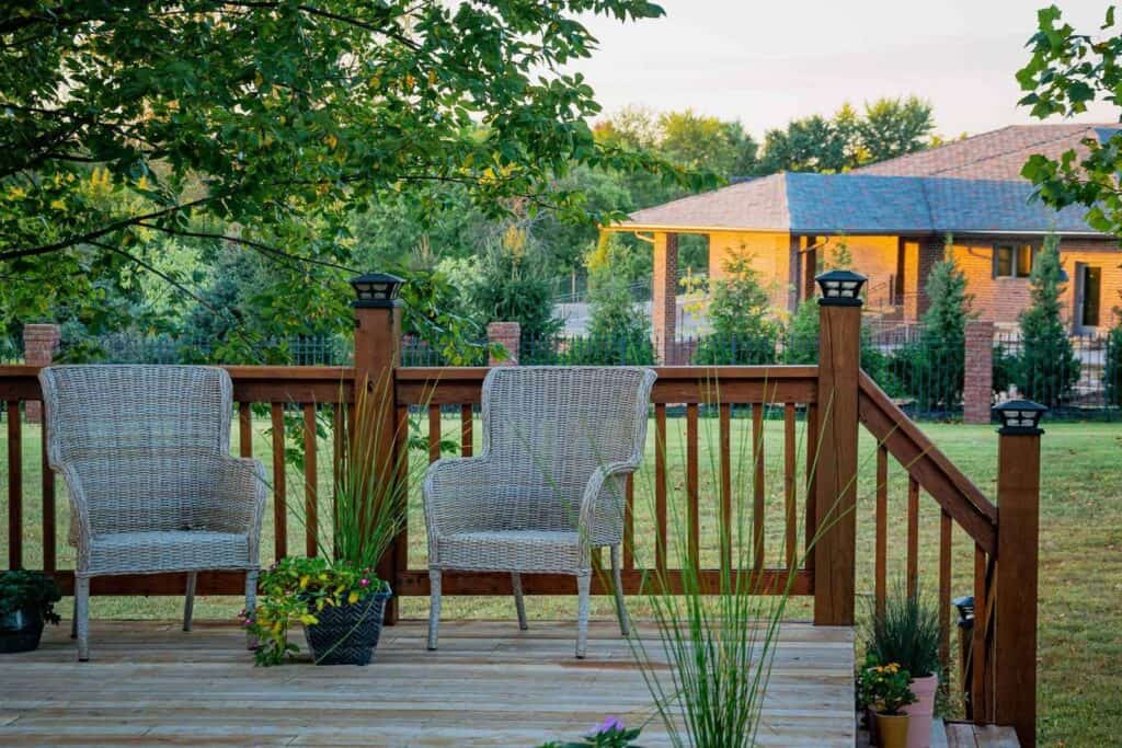 A family completes a home exterior upgrade with a beautiful outdoor backyard deck with plants and comfy wicker chairs.